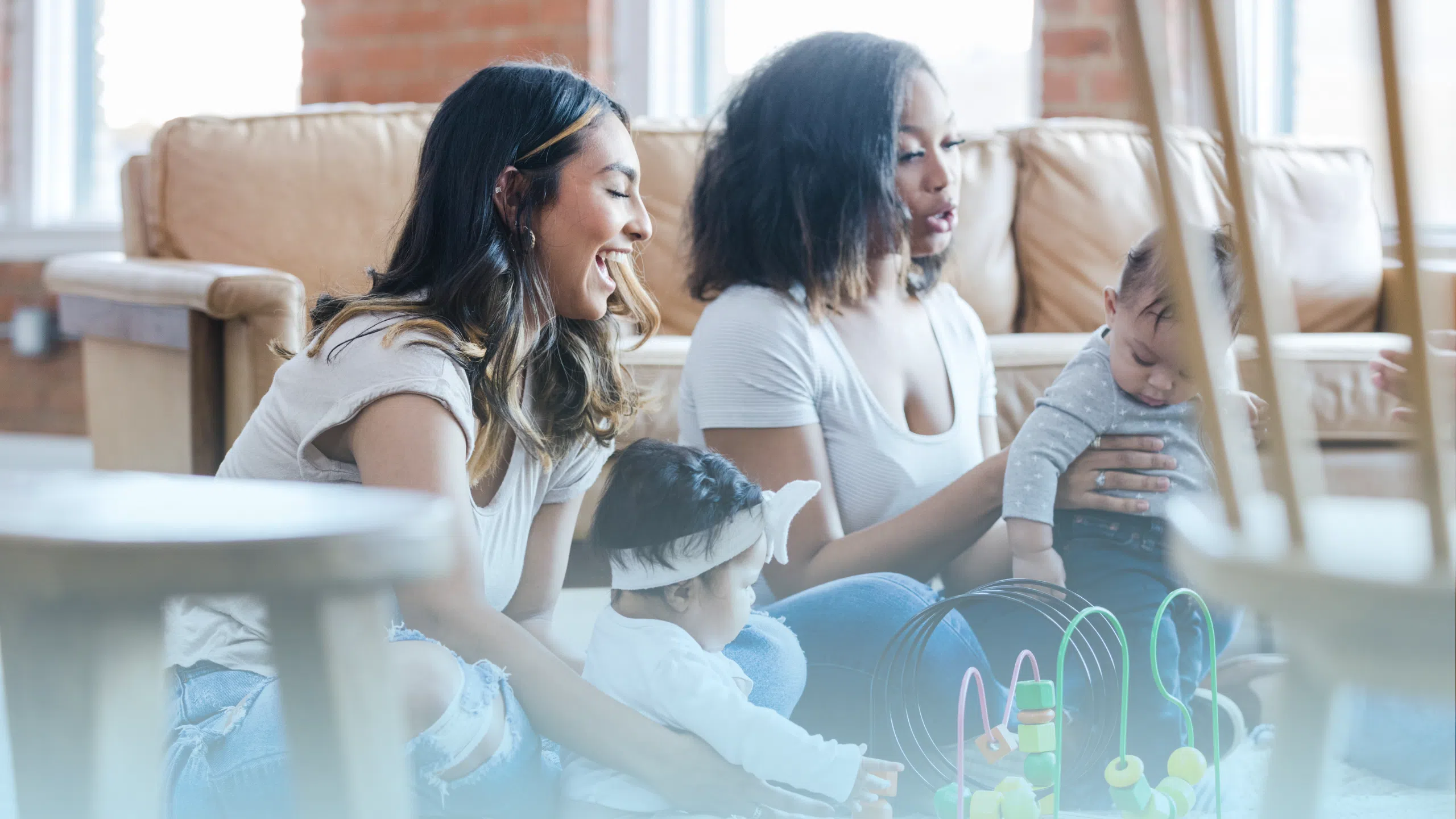 Two smiling mothers sitting on the floor playing with their babies during a postpartum support group.