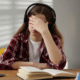 Stressed teenage girl with headphones holding her face while studying, illustrating teen back to school stress.