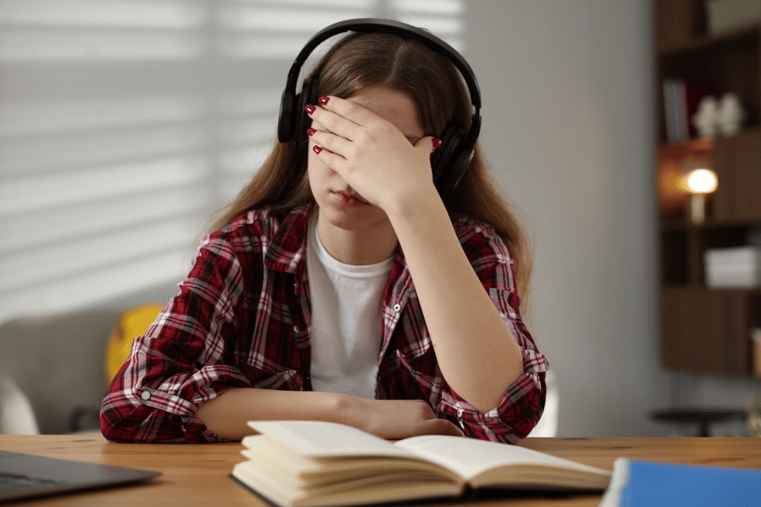 Stressed teenage girl with headphones holding her face while studying, illustrating teen back to school stress.