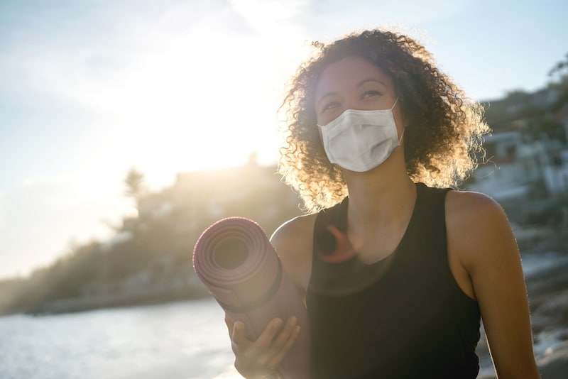 Woman with face mask to protect her from COVID-19 carrying yoga mat