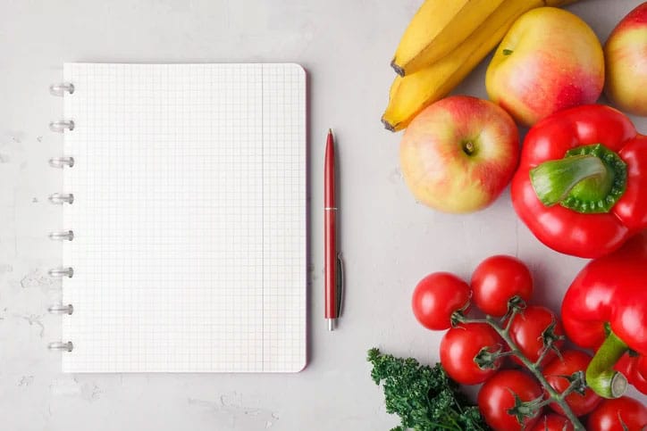 Fruits and vegetables next to notebook for tracking food to reach fitness goal
