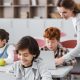Teacher-helping-schoolboy-working-on-laptop-during-lesson-blurred-background