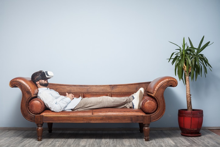 Man lays on couch with VR headset in a telehealth therapy session