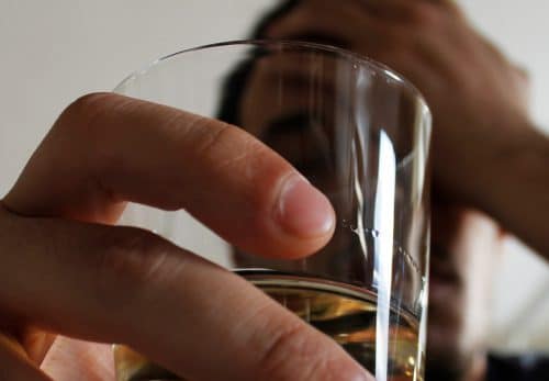 Man drinks a glass of whiskey battling addiction.