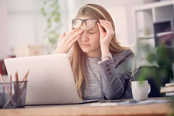 Tired woman rubs eyes while working on laptop computer