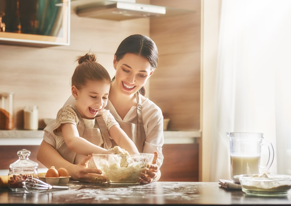 Young girl getting cognitive benefits by cooking with her mom in the kitchen