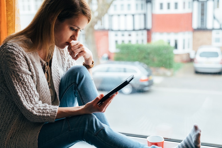 Woman looks at mobile device by herself, coping with COVID-19 anxiety and social distancing