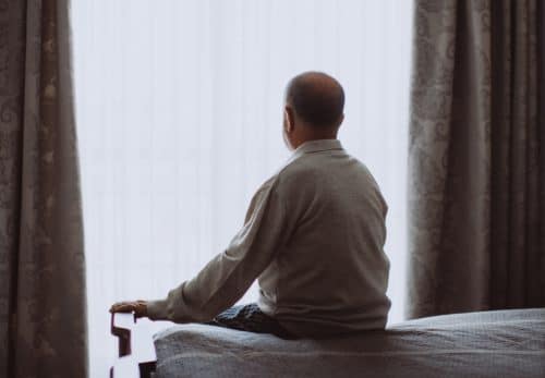 Man sits alone in dark bedroom struggling with adult depression.