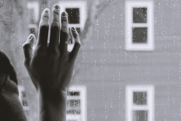 Hand up against rainy windowpane from person struggling with depression.