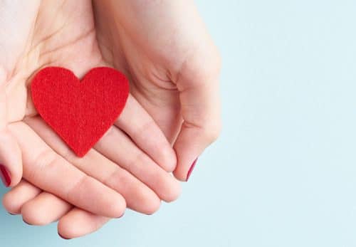 Woman holds cut out heart in hand symbolizing making a charitable donation.