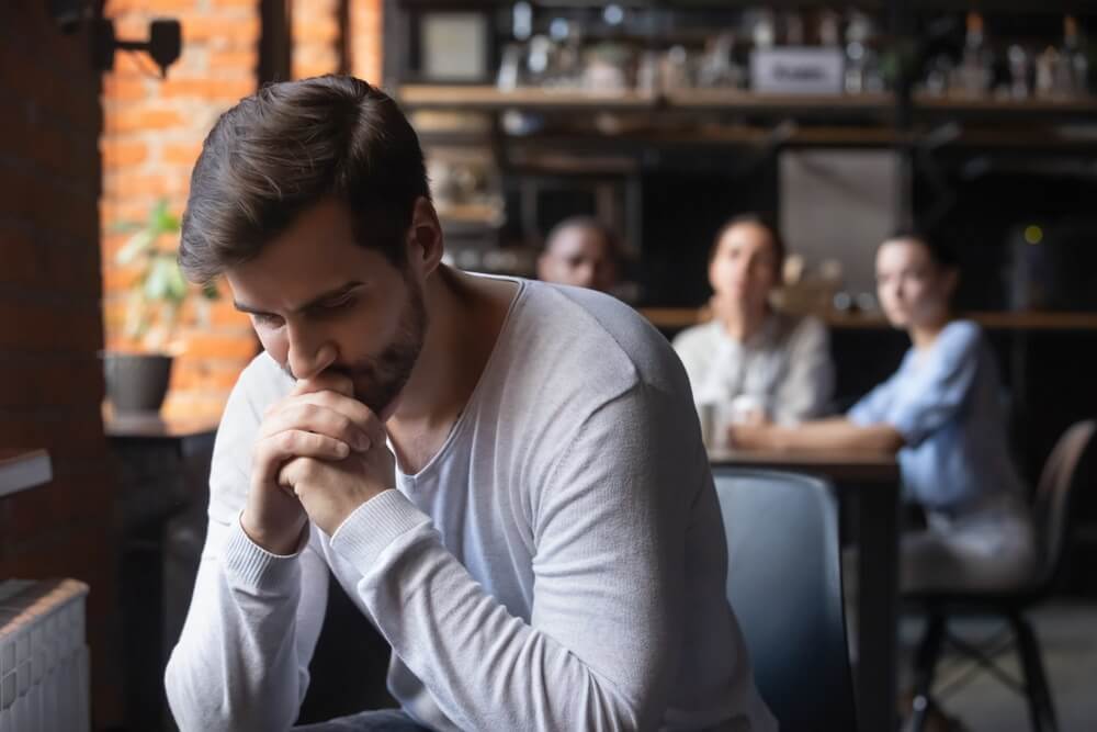 Man feeling disconnected and sitting alone with people looking on in the background
