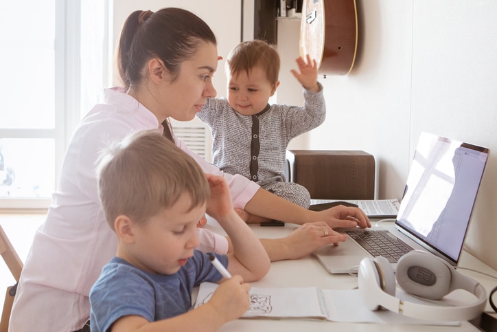 Woman tries to work on laptop with young children in need of Cognitive Behavioral Therapy to cope.