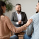 Marital Therapy Concept. Happy couple reconciling at session in therapists office during appointment, looking at each other, smiling woman touching man's shoulder, back view, selective focus