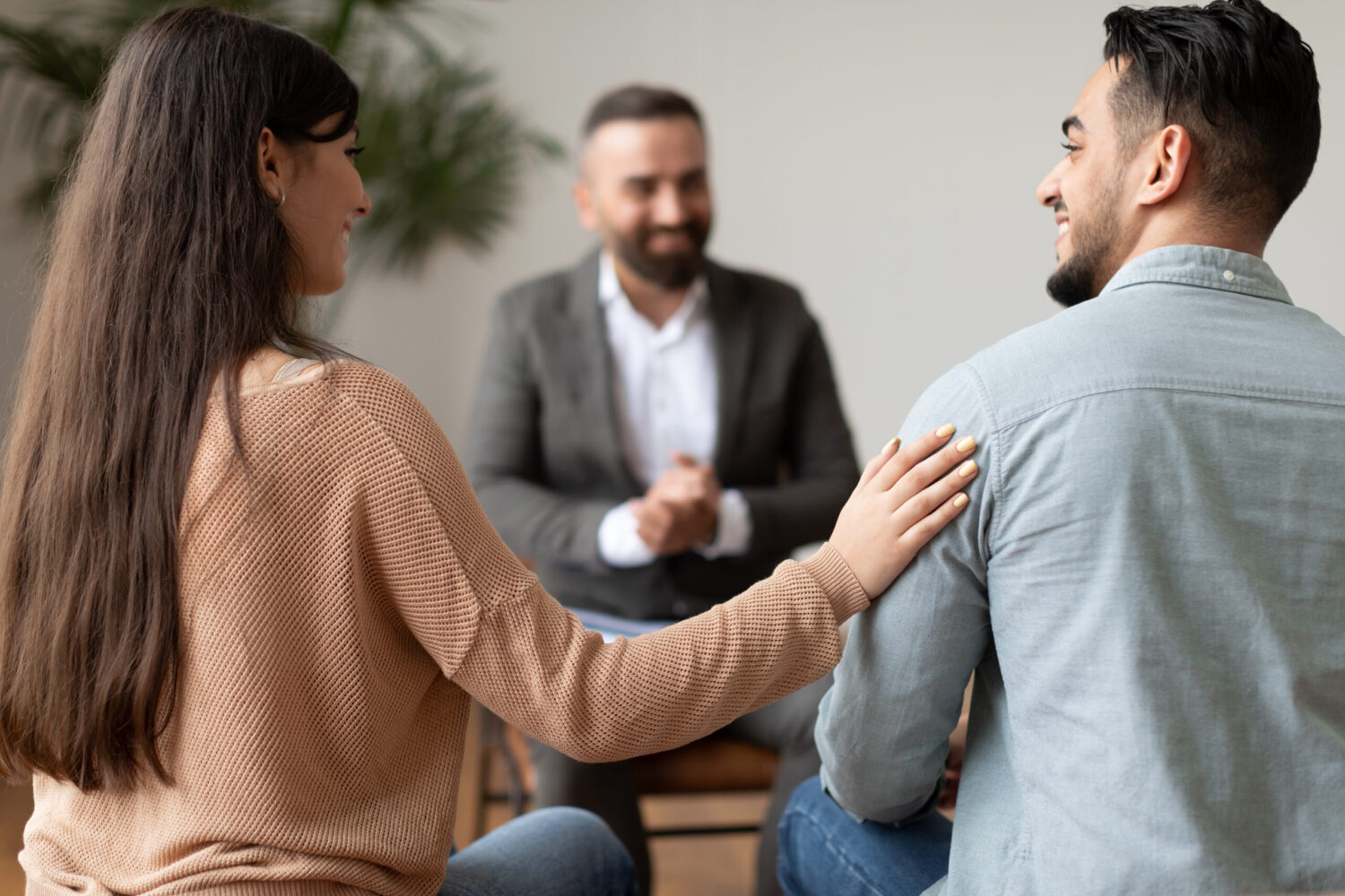 Marital Therapy Concept. Happy couple reconciling at session in therapists office during appointment, looking at each other, smiling woman touching man's shoulder, back view, selective focus