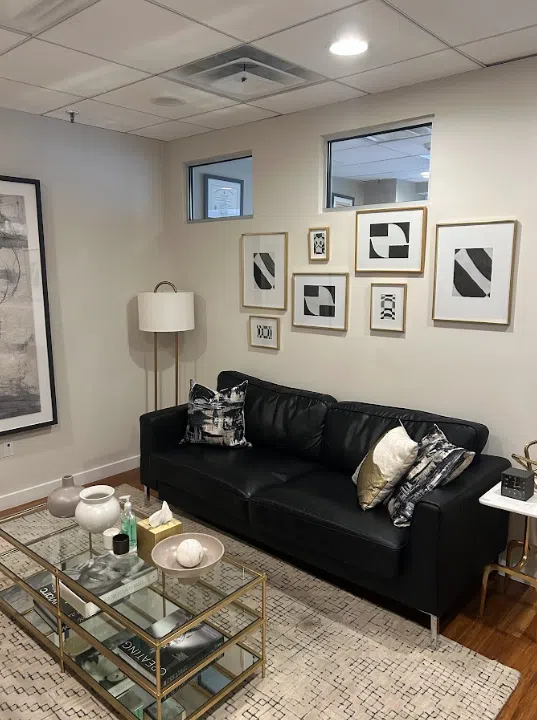 Therapy office with a black leather sofa and gallery wall of framed art at the Lukin Center Hoboken office
