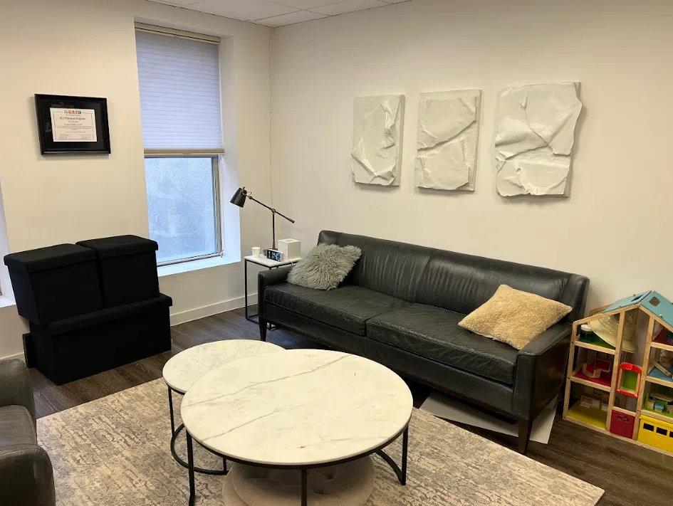 Family therapy room with a sofa, marble table, and children's play area at the Lukin Center Hoboken office