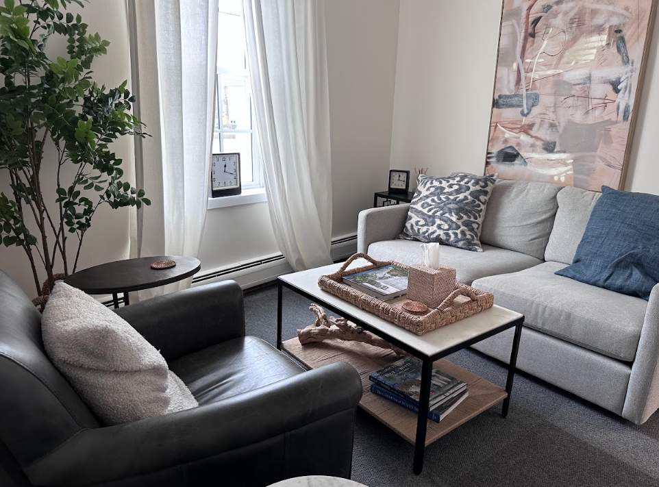 Therapy room with a gray sofa, leather armchair, and plant at the Lukin Center Montclair office