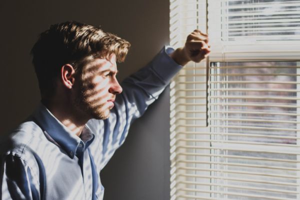Man in dark room looks out window in need of specialized men's therapy.