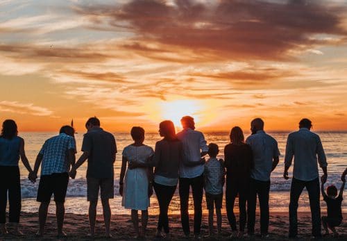 Large blended family holds hands on the beach watching the sunset.