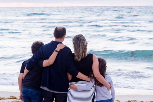 Blended family of four watches the waves on the beach.