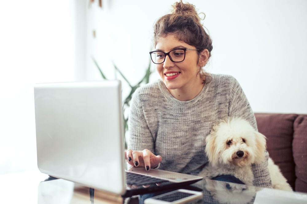 Woman works on laptop with dog on lap for mental health