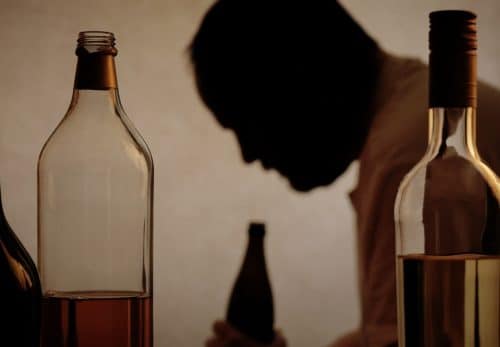 Man struggling with substance abuse surrounded by bottles of alcohol