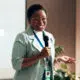 A woman holding a microphone and speaking at a world mental health day event.