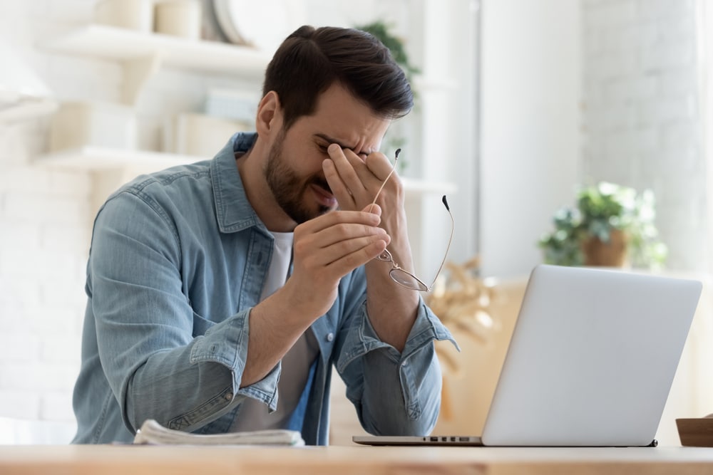 Tired man working on laptop suffering from Work From Home WFH Burnout